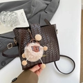 Brown woven leather bucket bag with lion pendant and gold logo on white surface - Brown with Pendant