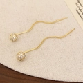 Detalle de pendientes largos dorados con esferas de circonitas brillantes sobre lino - Dorado