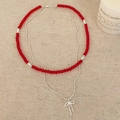 Double-layered necklace with red beads and a silver bow pendant on a linen surface - Red Glass Bead Style