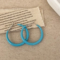 Detailopname van helderblauwe hars oorringen met gladde afwerking op vintage linnen doek - Blauw