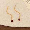 Detail van rode druppel oorbellen met gouden golfketting op een achtergrond van jute - Angola Rood