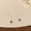 Macro-opname van zilveren kwastjes oorbellen met blauwgroen emaille op beige linnen - Pauwblauw