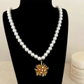Elegante collar de perlas con colgante de flor dorada en un soporte negro - Flor Dorada Perla Blanca