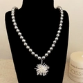 Elegante collar de perlas grises con colgante de estrella plateada en un soporte negro - Flor Plateada Perla Gris