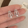 Orecchini a triangolo con zirconi micro-pavé e perle bianche appese su sfondo strutturato - Argento