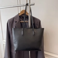 Minimalist black PU leather tote bag hanging against a neutral wall with suit background - Black
