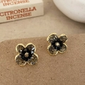 Detail of flower stud earrings with gold frames and dark crystals on earthy paper - Black Flower Stud Earrings