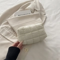 Quilted cream vanity pouch with zipper closure placed on stylish blazer and book - White