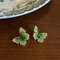 Close-up of green crystal butterfly earrings with gold plating on wooden texture background - Green