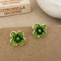 Detalle macro de pendientes de trébol con piedras verdes y base de metal dorado - Verde