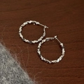 Detalle macro de pendientes de aro plateados con textura geométrica en madera vintage - Pendientes de aro de plata triturada plateada