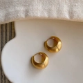 Dettaglio di orecchini a cerchio a C dorati spazzolati su un vassoio di ceramica bianca - Oro