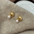 Dettaglio di orecchini a perla dorata appoggiati su un morbido tessuto a maglia beige - Orecchini con Perle ad Alta Lucentezza Oro