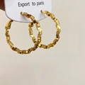 Dettaglio di grandi orecchini a cerchio dorati con trama geometrica a strati - Oro
