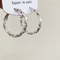 Dettaglio macro di grandi orecchini a cerchio argento con trama sfaccettata irregolare - Argento