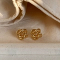 Primer plano de pendientes de botón con nudo retorcido dorado sobre tela suave - Dorado