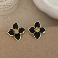 Detailed macro of black four-petal flower earrings with golden bead centers on craft card - Black