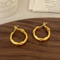 Dettaglio di orecchini a cerchio intrecciati color oro opaco su vassoio in legno - Oro Opaco