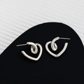 Vue macro des boucles d'oreilles cœur torsadées en argent sur un présentoir noir chic - Argenté