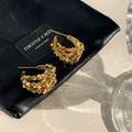 Détail des boucles d'oreilles multicouches dorées sur pochette chic en cuir noir - Doré