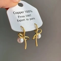 Primer plano de pendientes de lazo dorado con perlas blancas en tarjeta de cobre puro - Pendientes de Botón de Perla con Lazo Dorados