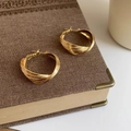 Primer plano de pendientes de aro dorados retorcidos con diseño de espiral en un libro - Dorado