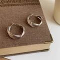 Detalle de pendientes de aro plateados y retorcidos sobre un libro de estilo vintage - Plateado