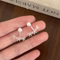 Primer plano de pendientes de lazo plateados con perla blanca sostenidos con la mano - Estilo Lazo / Plateado