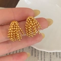Golden cluster tassel earrings with sphere bead design shown in a hand close-up - Gold