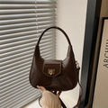Bolso hobo media luna en charol marrón oscuro con hebilla dorada sostenido en mano - Marrón