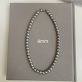 Detalle de un collar de perlas grises de 8mm con cierre plateado sobre fondo textil - Estilo 8mm / Gris
