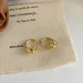 Minimalist gold knotted chain huggie earrings displayed on a textured fabric background - Gold