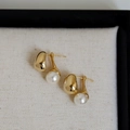Detailed view of elegant gold bean studs with white round pearl drops on a textured fabric - Gold