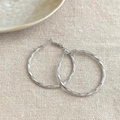 Schicke silberne geometrische Creolen mit Spiralstruktur auf natürlichem Leinenhintergrund - Ring mit Spiralstruktur / Silber