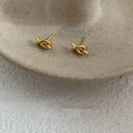 Close-up of polished knot-shaped gold earrings on a textured stone display tray - Gold