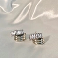 Detailed close-up of layered gold stud earrings with rectangular zircon on silk background - Silver
