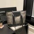Chic taupe suede tote bag with black trim, styled in a minimalist city cafe setting - Black