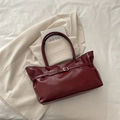 Deep red patent leather tote bag with gold buckle on a white minimalist background - Red