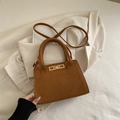 Elegant brown matte suede handbag with gold lock placed on a beige blazer stylish display - Brown