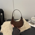 Brown suede crescent bag with leather trim and gold zipper shown in a cozy home setting - Brown