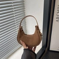 Bolso media luna de ante marrón con detalles dorados y asa minimalista bajo luz natural - Caqui