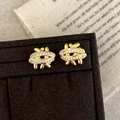 Macro view of gold-tone braided stud earrings with pave-set cubic zirconia on a stand - Gold