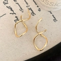Detailed view of luxury gold geometric wave earrings on textured linen background - Gold