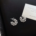 Irregular silver C-shaped stud earrings with wire-wrap detail on a black leather background - Silver