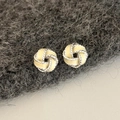 Macro shot of silver twisted knot stud earrings with creamy white enamel inlay details - Yellow