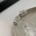 Macro detail of silver multi-layered textured ear cuffs on a ceramic tray edge - Silver Textured Four-Claw Stud Earrings