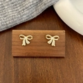 Close-up of gold bow earrings with micro-pave zircons displayed on a dark wood stand - Bowknot Stud Earrings / Gold