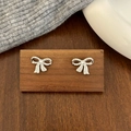 Close-up of silver bow stud earrings with sparkling pavé zircons on a wooden display - Bowknot Stud Earrings / Silver