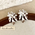 Détail de boucles d'oreilles fleurs argentées avec texture martelée sur support en bois - Argenté