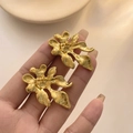 Elegante goldene Blüten-Ohrstecker mit metallischem Glanz, zur Maßstabsanzeige in der Hand - Gold
